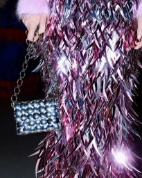 Close-up of a person wearing a shimmering metallic fringed garment and holding a studded silver shoulder bag with chain strap.