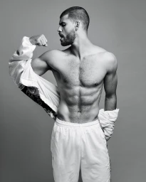 Monochrome portrait of a muscular shirtless man flexing his bicep while wearing white athletic trousers.