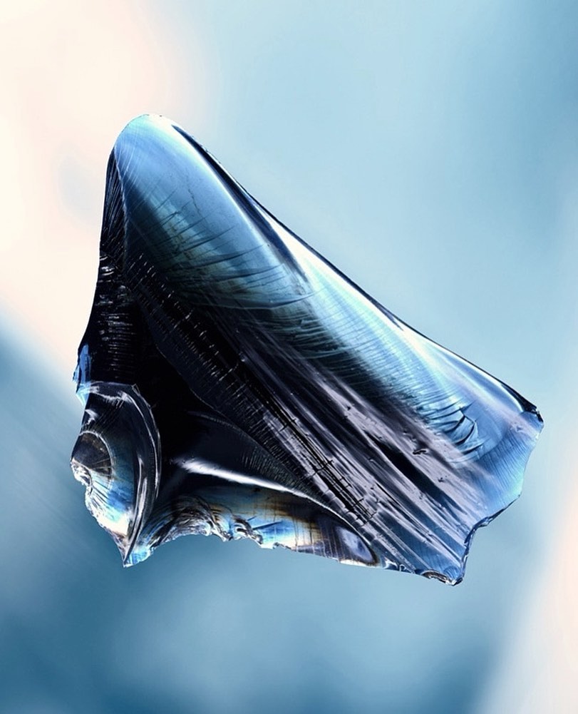 Abstract image of a dark blue translucent shard reflecting light against a blue background with subtle color gradients and light reflections.