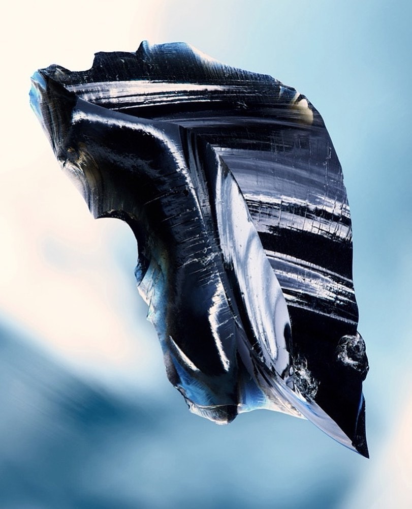 Abstract obsidian rock fragment with visible internal structures, illuminated against a soft blue gradient background for graphic design.