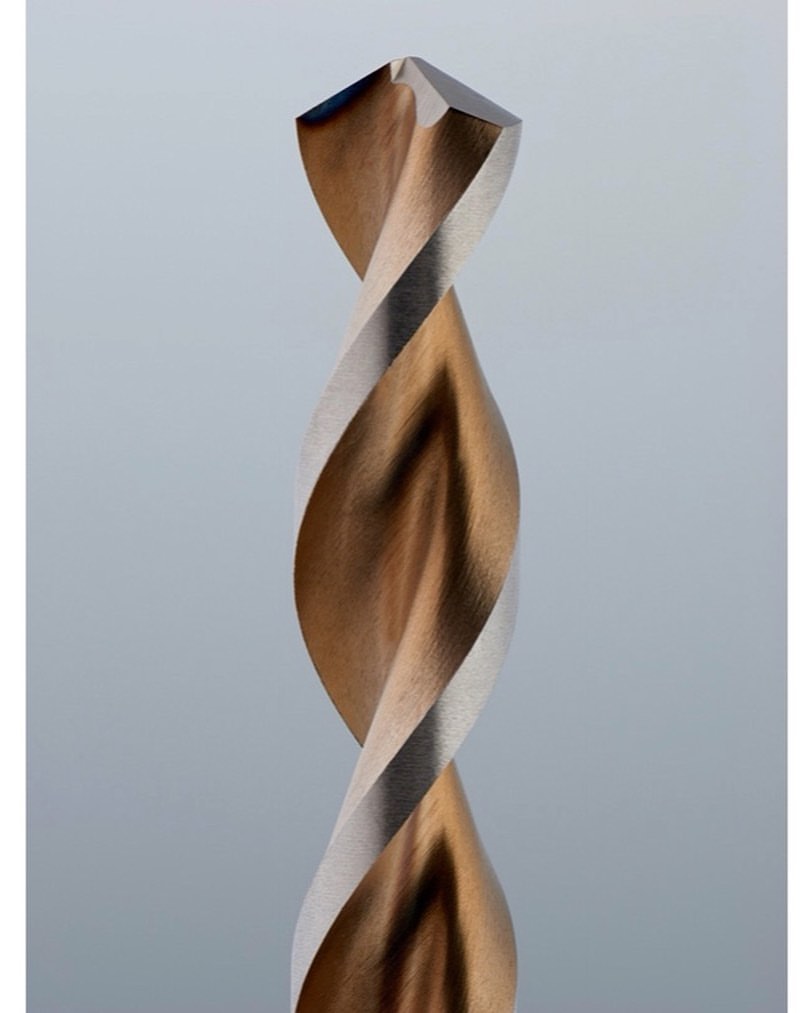 Close-up of a metal drill bit showing the twisted flutes and sharpened tip against a light grey background, suitable for engineering.