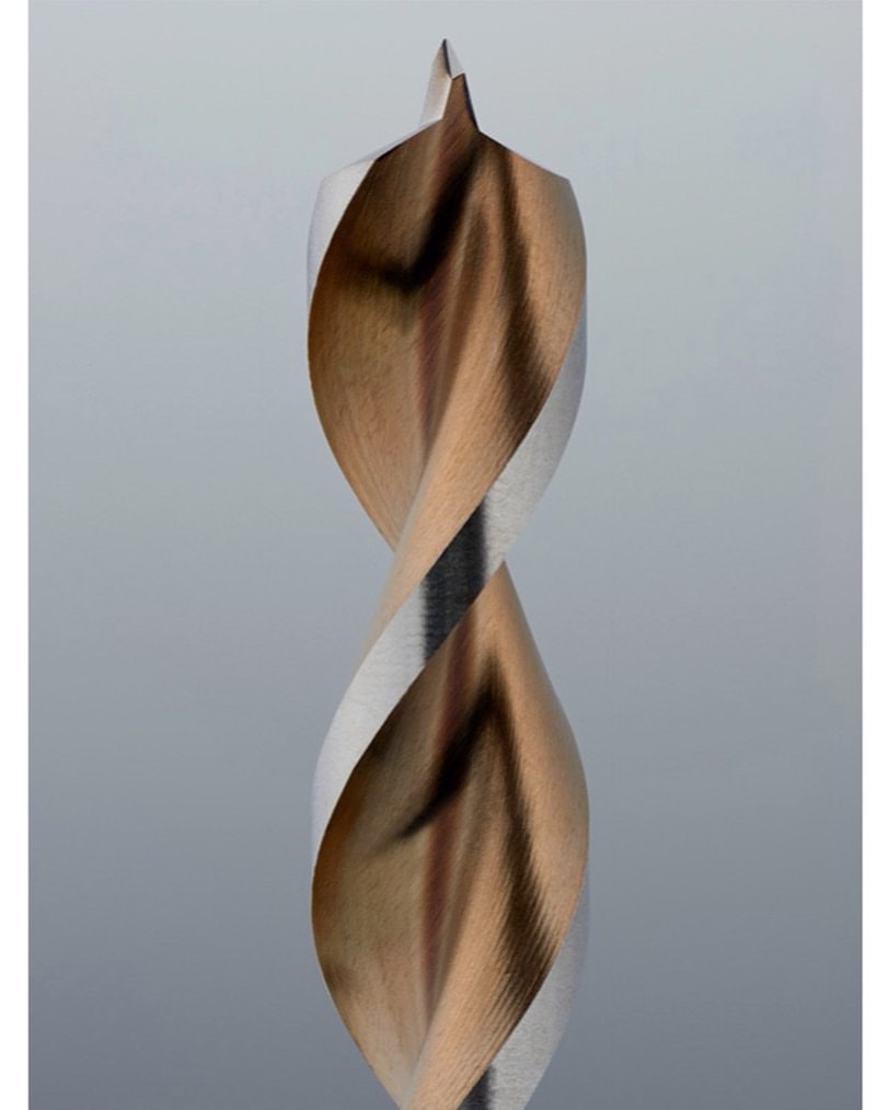 Close-up of a two-toned metal drill bit with a twisted design and pointed tip, set against a neutral grey background, showcasing precision engineering.