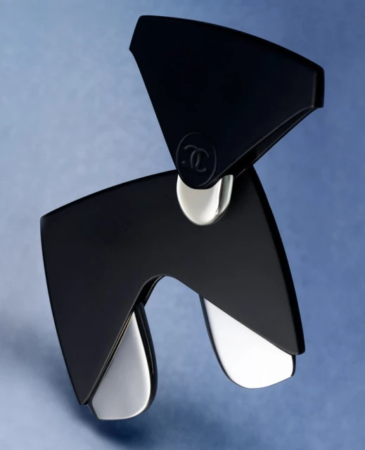Stylish black and silver brooch featuring the iconic Chanel logo, set against a soft blue backdrop, perfect for luxury fashion accessory.