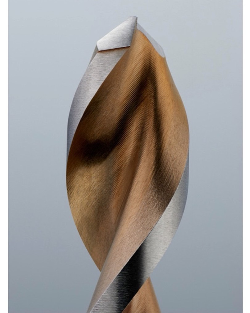 Close-up studio shot of a drill bit with a bronze-colored body and silver edges. The drill bit is set against a plain grey background.
