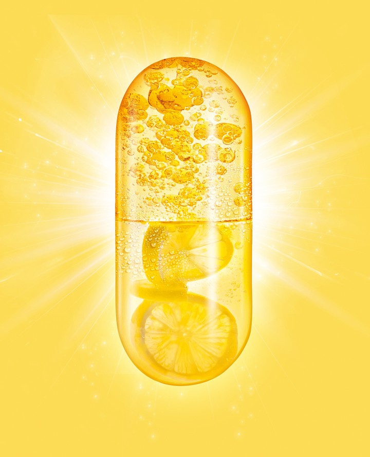 Vitamin C capsule close-up on a yellow background. Clear gel capsule filled with liquid and floating lemon slices.