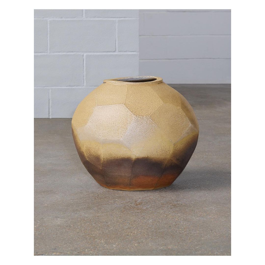 Neutral-toned ceramic vase with geometric facets, featuring a dark brown ombre effect and minimalist design, on a gray surface against a brick wall.