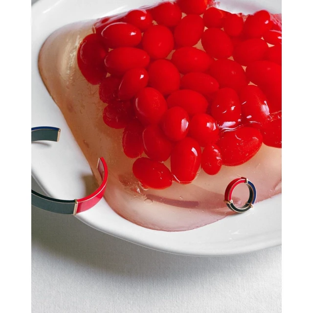 Overhead studio shot of fruit jelly with red fruit pieces and fashion bracelets on a white plate and light grey surface.