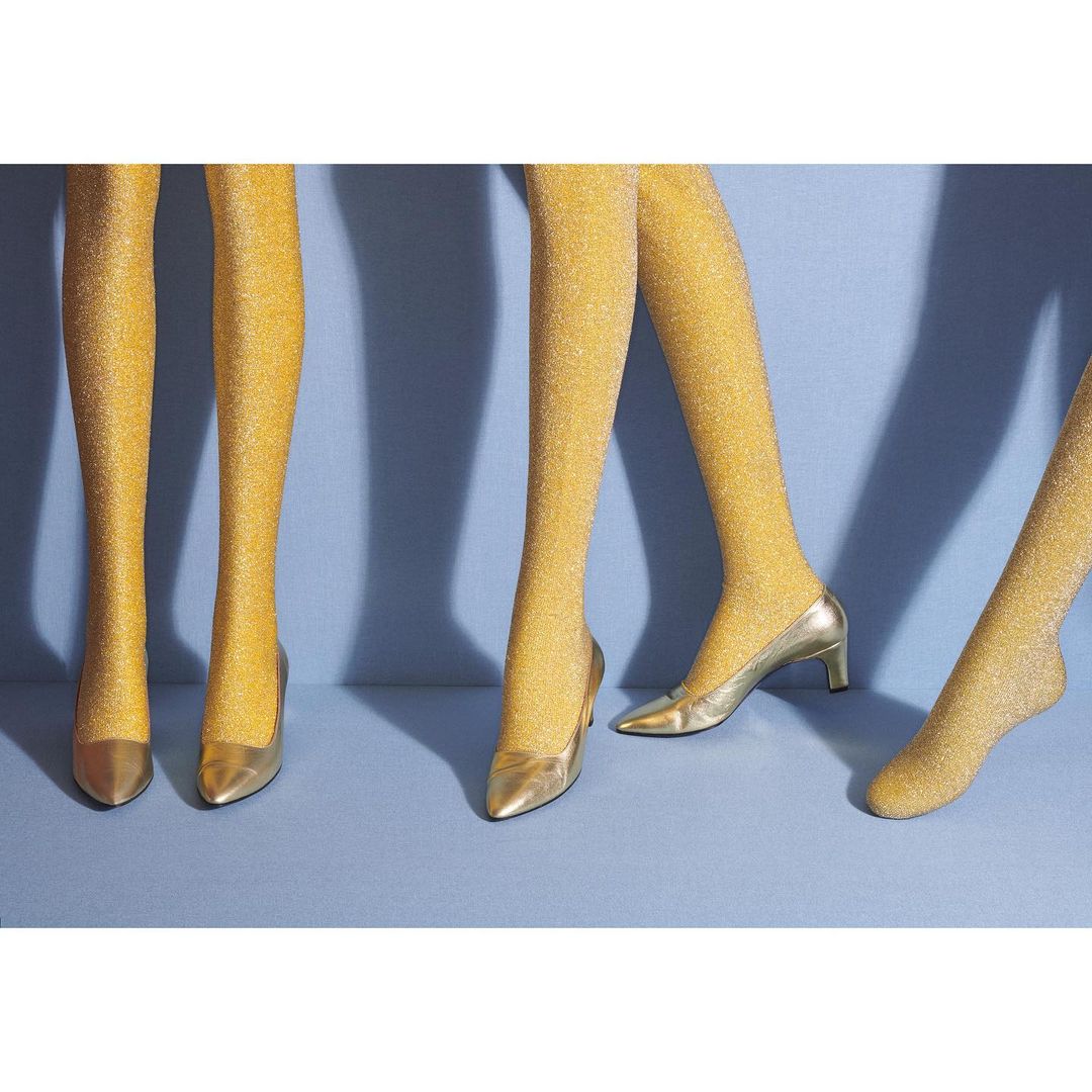 Three pairs of mannequin legs wearing glittery gold tights and matching gold high heels on a light blue background.