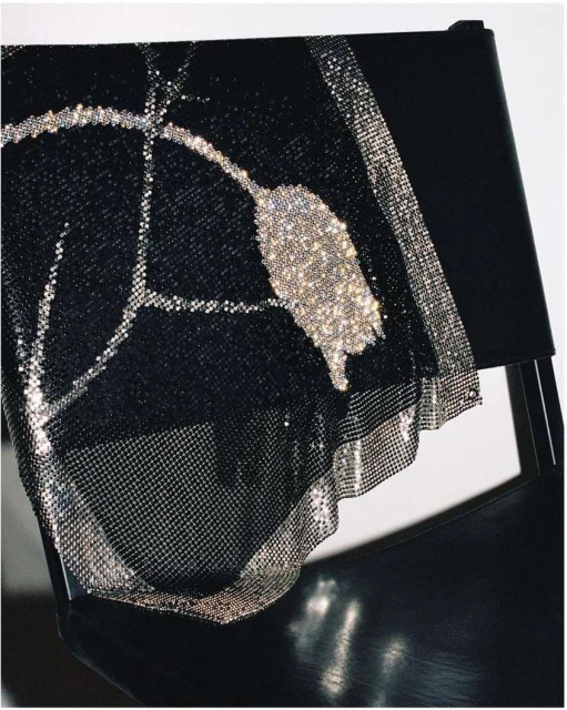 Close-up of a black dress with silver sequins draped over a black chair, against a neutral background. Fashion, texture, and design are featured.