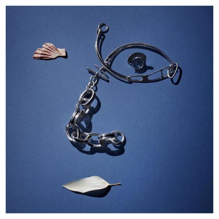 Overhead shot of silver chain necklace, ring, leaf, and seashell arranged on a blue background, illuminated by a strong light source.