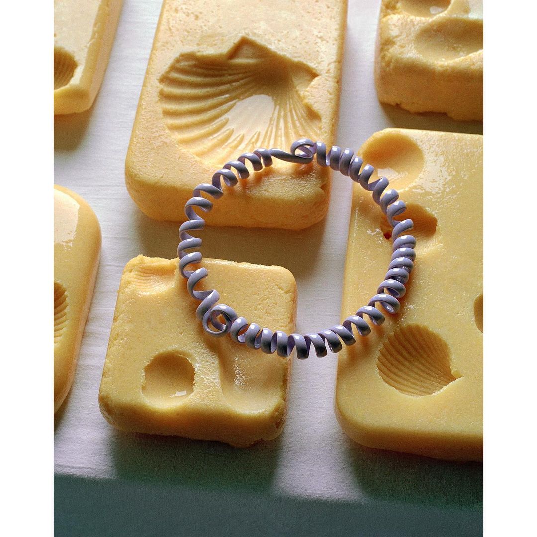 Overhead shot of artisanal soaps with seashell imprints and a lilac-colored, spiral hair tie, set against a clean, bright background.