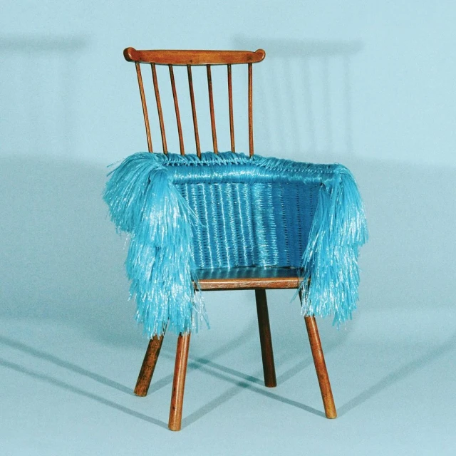 A wooden chair with a blue woven seat and blue fringe is set against a gradient blue background. The chair has a wood frame and legs.