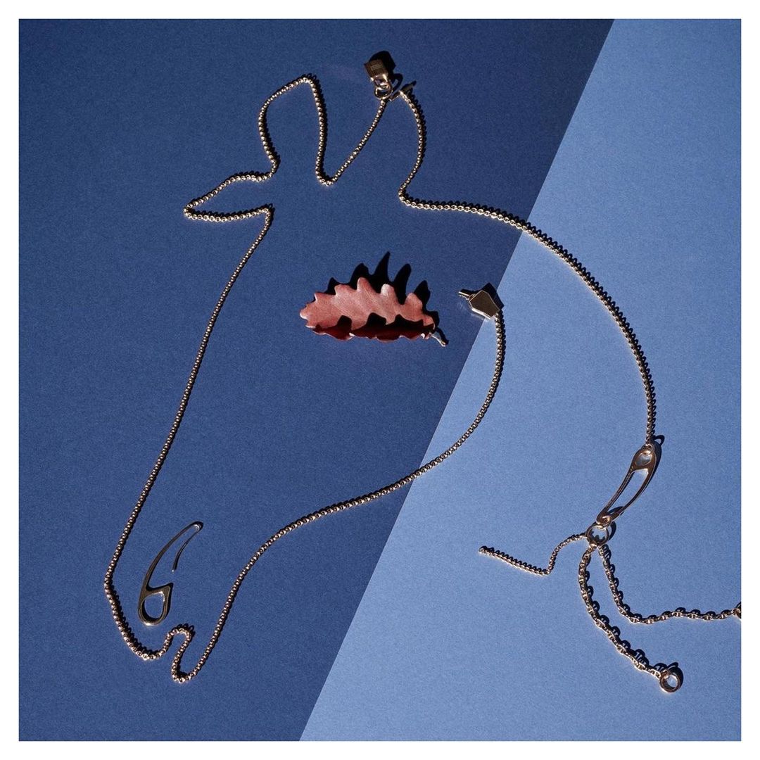 Silver chain necklace and autumn leaf on blue split background, minimalist jewelry still life, top-down studio product shot.