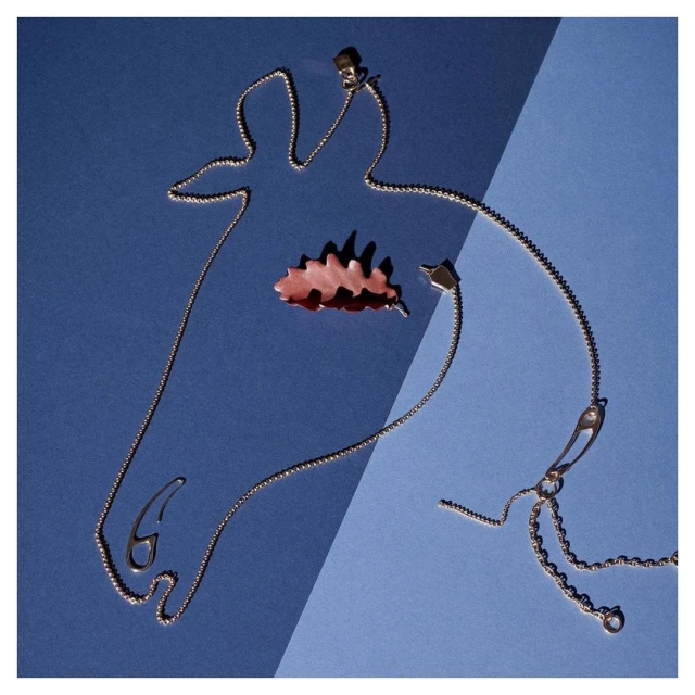 Silver chain necklace and autumn leaf on blue split background, minimalist jewelry still life, top-down studio product shot. 