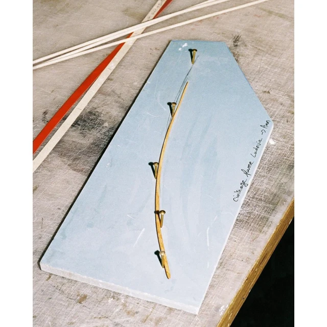 Craft project featuring a blue board with tacks securing a bent wooden slat, surrounded by light-colored rods, showcasing artistic construction.
