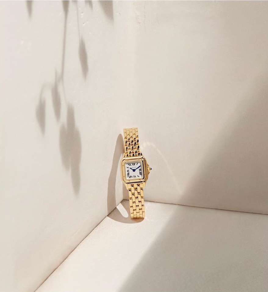 Elegant gold wristwatch on a light beige surface with a soft plant shadow creating a minimalist aesthetic for watch product photography.