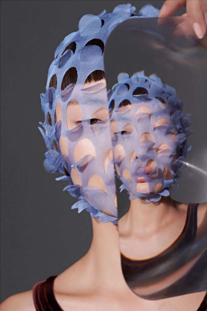Artistic portrait of a woman with a blue patterned veil overlay, set against a gray background in a studio with diffused lighting.