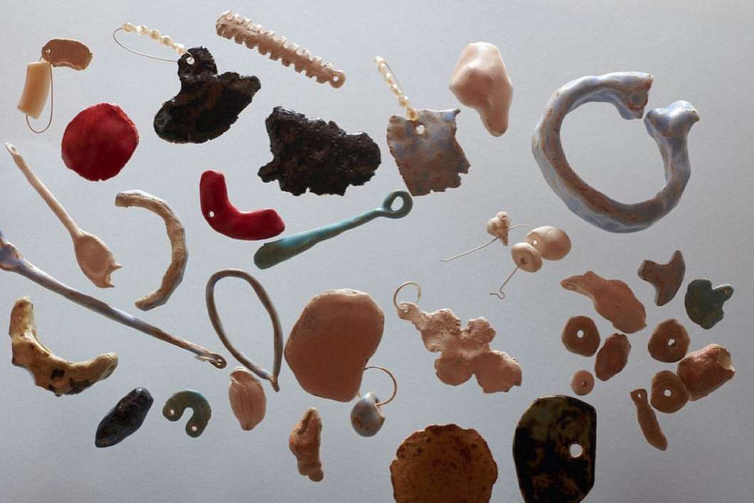 Collection of handmade clay pendants and charms in various shapes and colors, artfully arranged on a clean, light background.