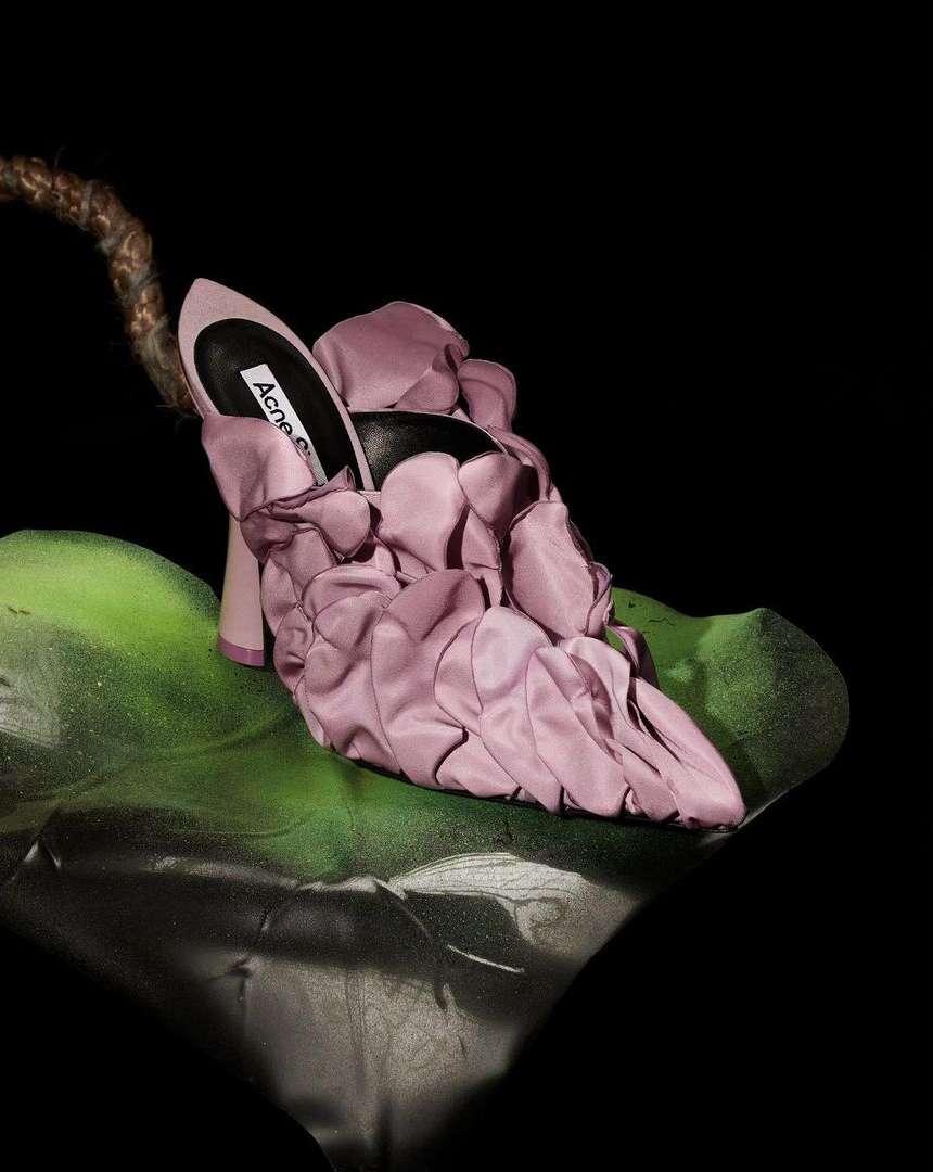 Silk floral high heel shoe by Acne Studios sits on a green leaf against a dark backdrop in a studio product shot for fashion.