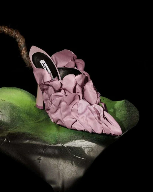 Silk floral high heel shoe by Acne Studios sits on a green leaf against a dark backdrop in a studio product shot for fashion.