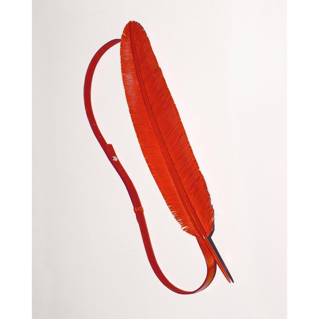 An orange feather with a strap attached to its base, presented on a white backdrop to showcase the material and design.