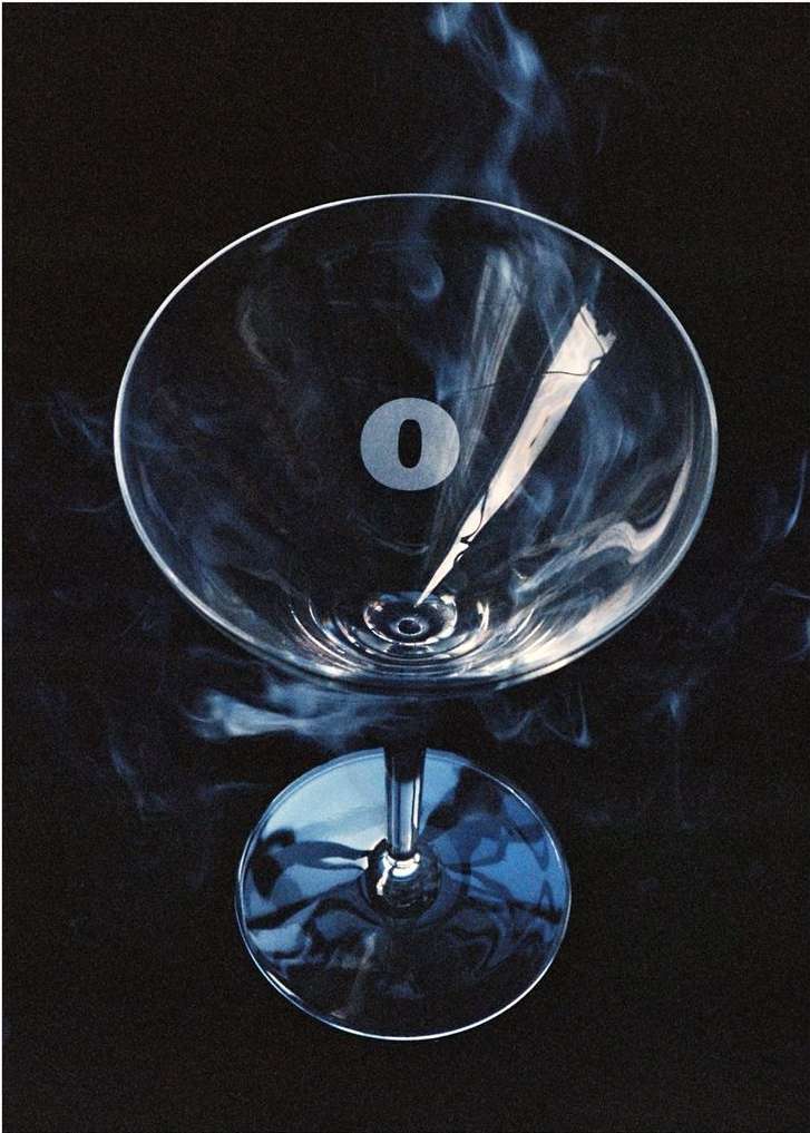 Dramatic studio shot of a martini glass partially filled with liquor and surrounded by blue smoke, set against a dark background.