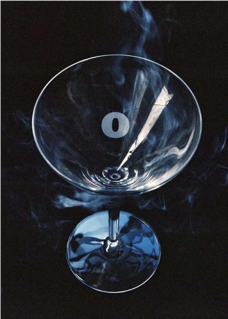 Dramatic studio shot of a martini glass partially filled with liquor and surrounded by blue smoke, set against a dark background.