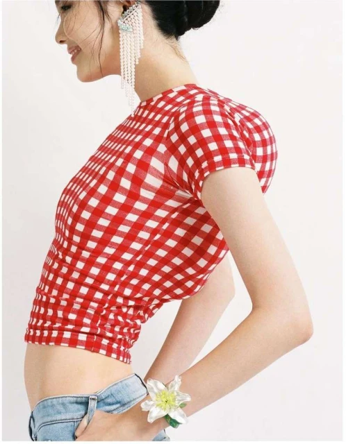 A woman in a red and white gingham crop top poses against a white background, showing off her casual style with light blue denim shorts.
