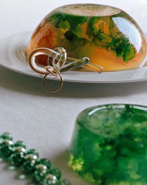Gelatin dessert on a white plate with decorative glass keys, beads, and a small green gelatin dessert on a white tablecloth.