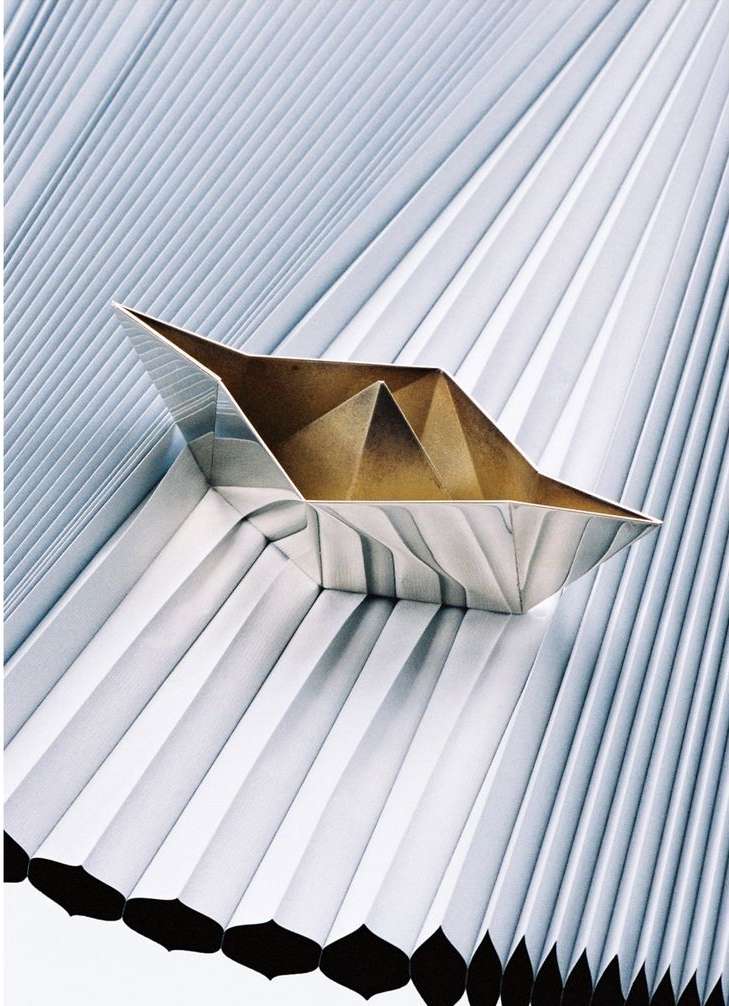 Abstract origami paper boat resting on a background of folded paper, creating a geometric pattern with metallic and neutral tones.