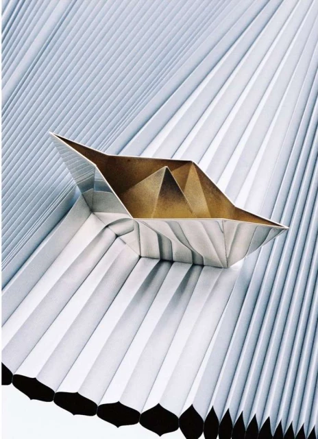 Abstract origami paper boat resting on a background of folded paper, creating a geometric pattern with metallic and neutral tones.
