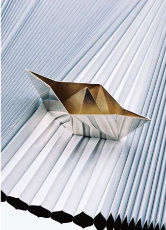 Abstract origami paper boat resting on a background of folded paper, creating a geometric pattern with metallic and neutral tones.