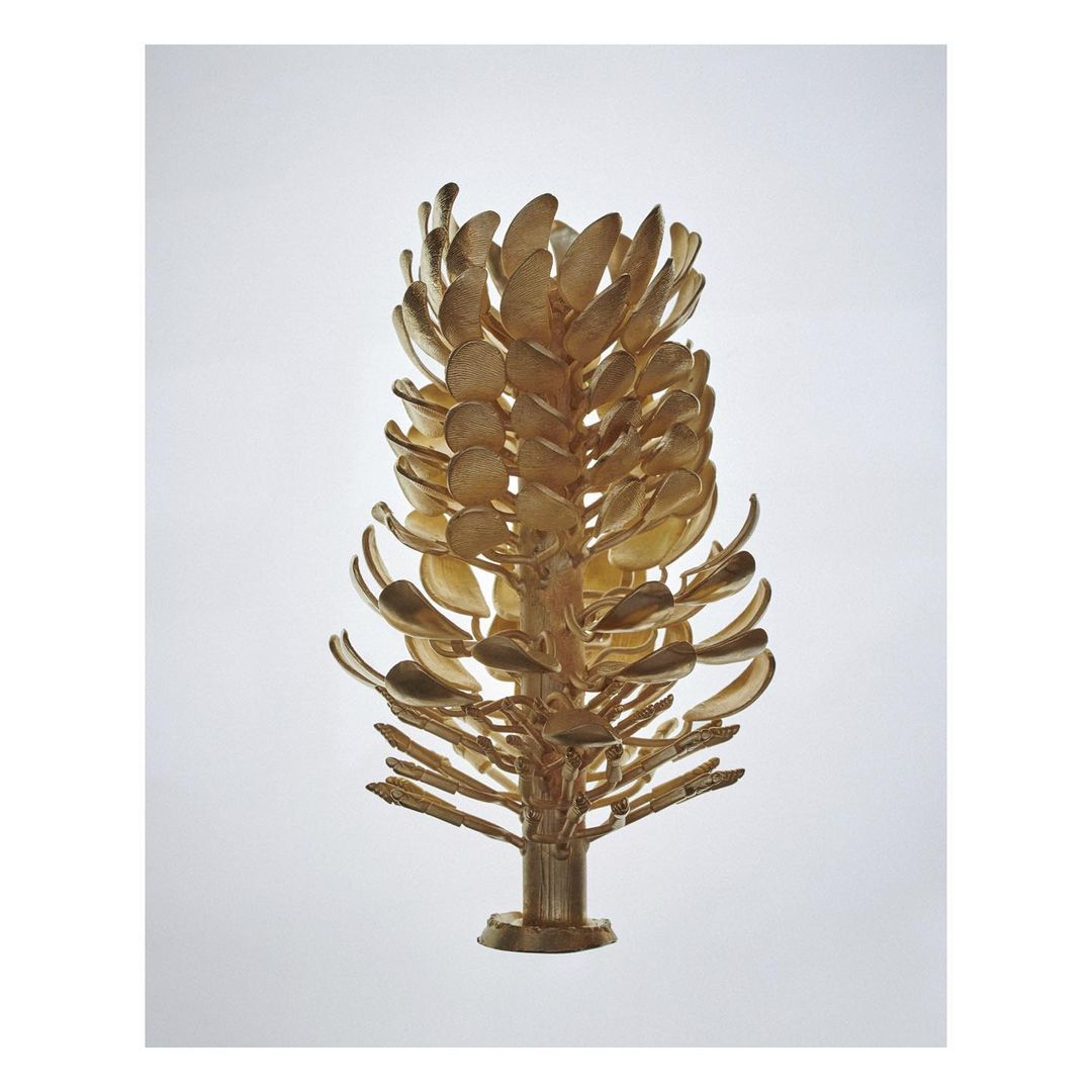 Golden metal casting tree structure against a plain white background, emphasizing its intricate branching and sculptural form.