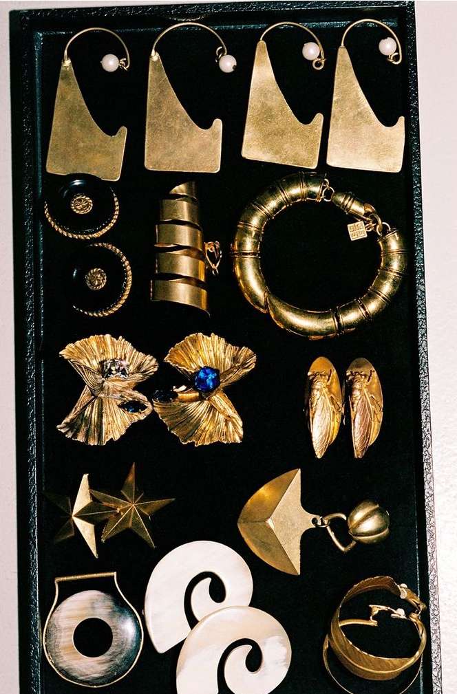 Close-up of assorted gold jewelry, including earrings, rings, a bracelet, and brooches displayed on a black tray. Jewelry fashion.