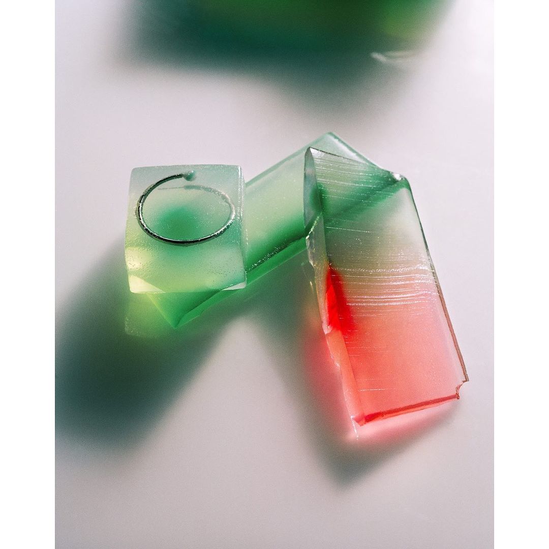 Geometric shapes in shades of green, white, and red with a silver ring embedded in a translucent green cube on a white surface.
