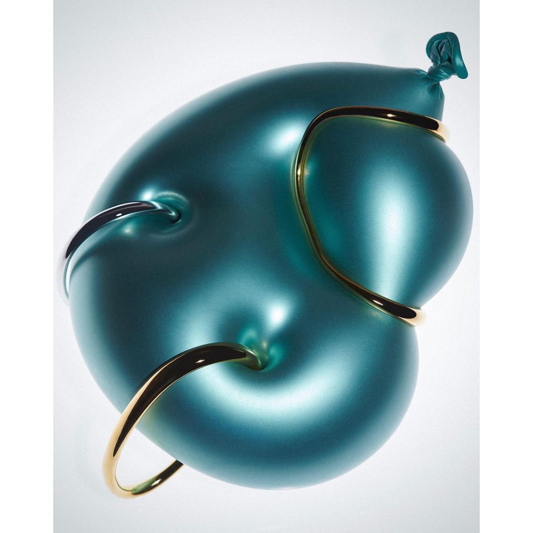 Close-up of an inflated teal balloon with several gold and silver metal rings piercing through it on a light, gradient background.