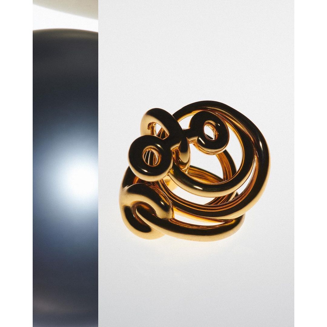 Abstract golden metal sculpture on a white background with a grey metallic orb on the left side in a minimalist style.
