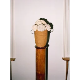 A woven basket filled with white cauliflowers sitting atop a polished wooden column against a plain wall.