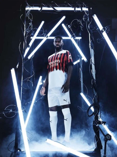 Adult male soccer player in uniform posing inside a custom light display in a studio with artificial fog at ground level.
