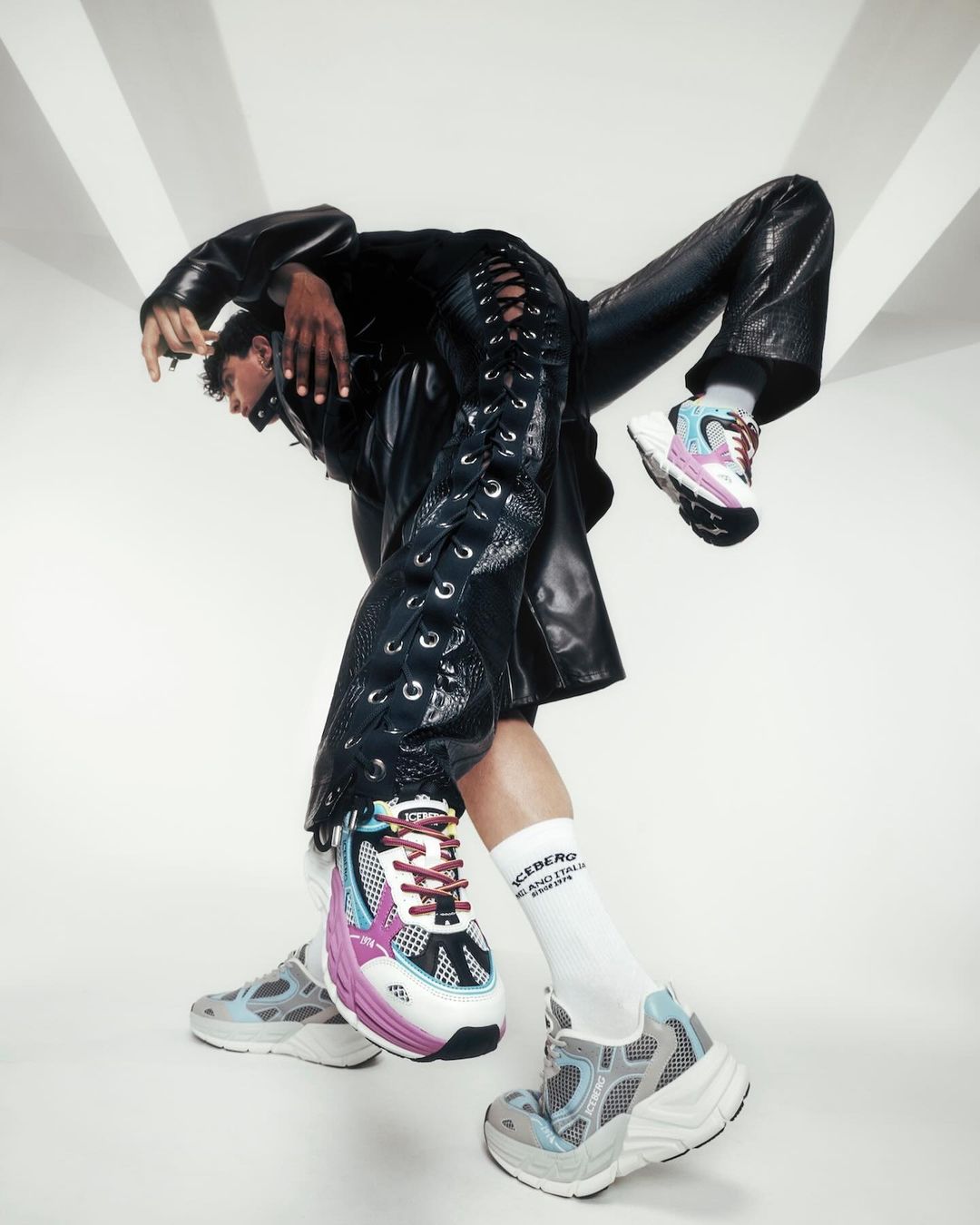 Fashionable shoes by Iceberg on a person wearing shiny black pants in a studio with bright lighting and white background.
