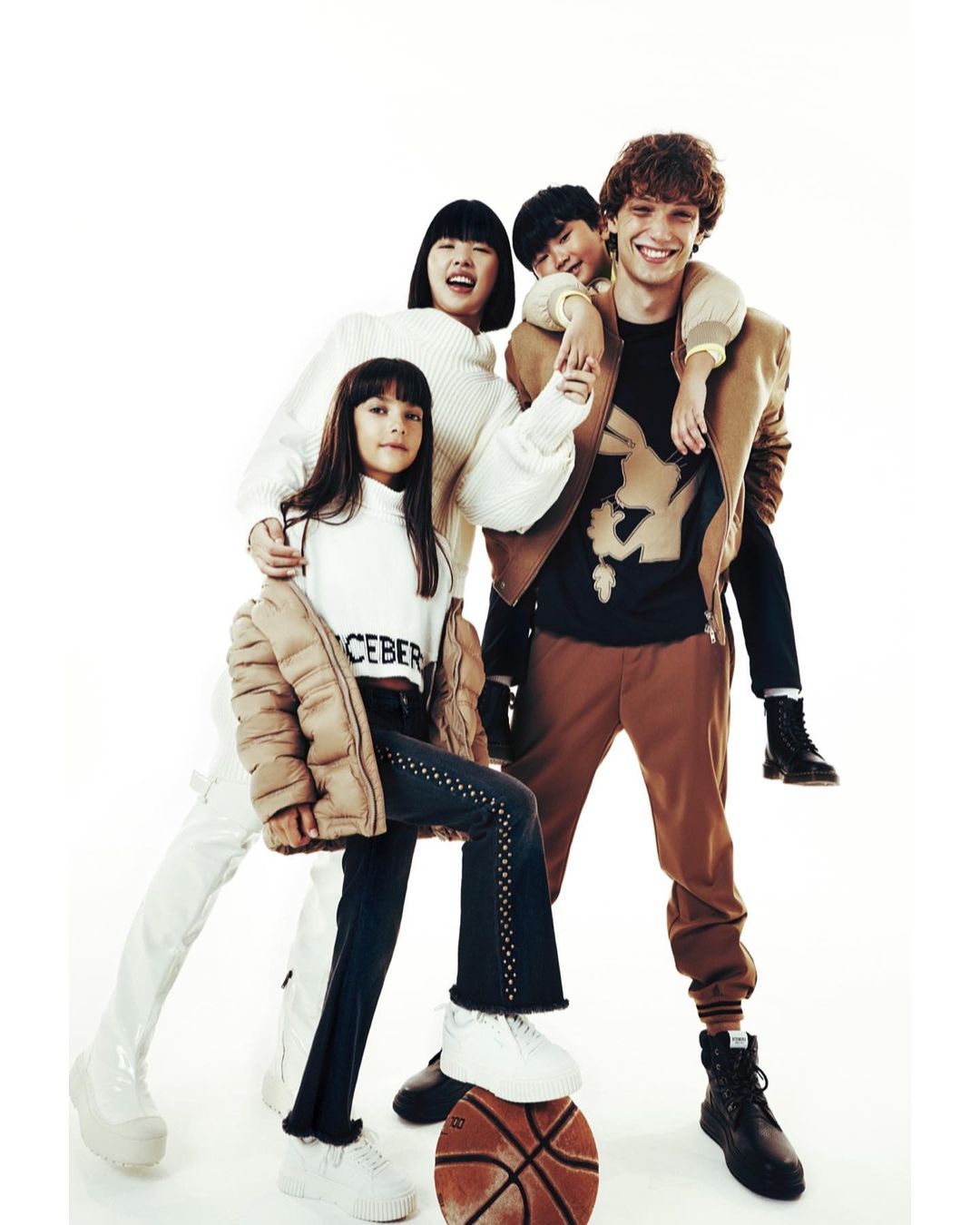 Four young people in stylish casualwear gather in a bright, eye-level studio shot featuring a basketball, promoting youth fashion.