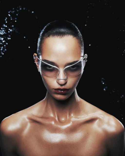 Close-up portrait of a woman wearing futuristic sunglasses with a jeweled frame against a dark background with bokeh-like highlights.