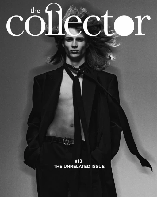 Magazine cover photo featuring a slender male model with long hair, wearing a blazer and tie, against a grey backdrop.