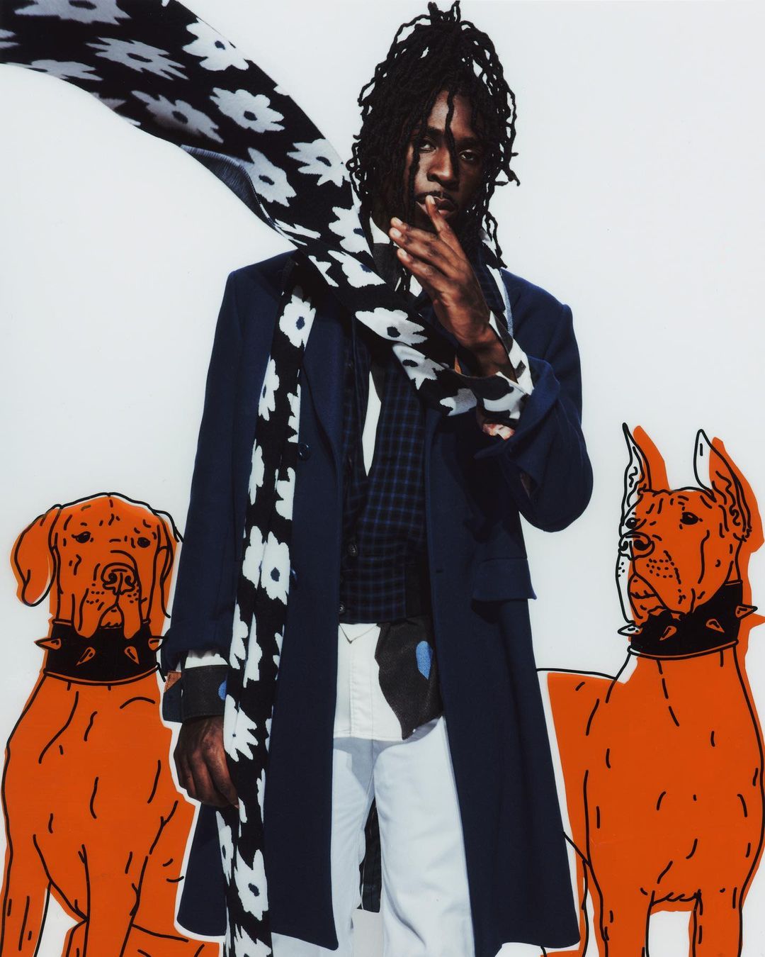 Stylish male model in coat, floral scarf poses with orange cartoon dog graphics on a white backdrop, fashion editorial photography.