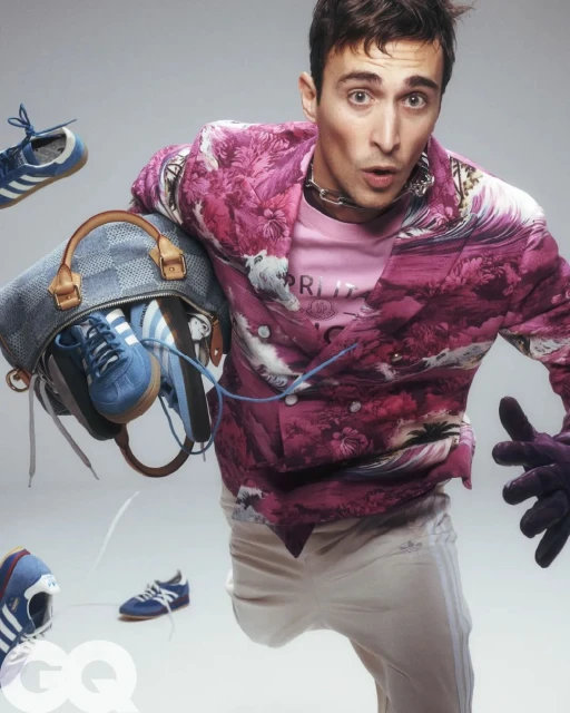 Stylish man in patterned jacket carries a bag with sneakers, with shoes floating around him against a neutral backdrop in a studio shot.