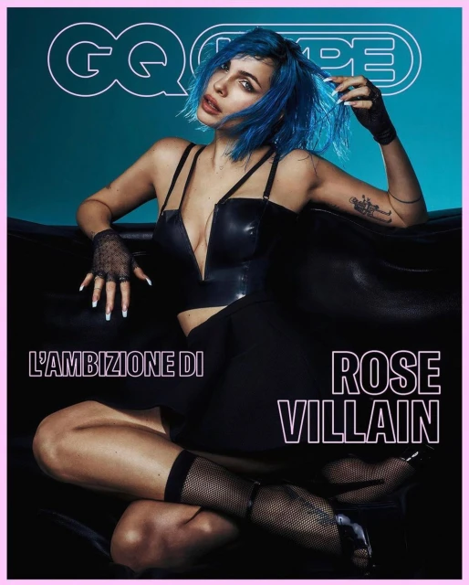 Rose Villain on the cover of GQ Type. Seated pose, wearing black corset top and skirt, blue hair, fishnet stockings, high heels.