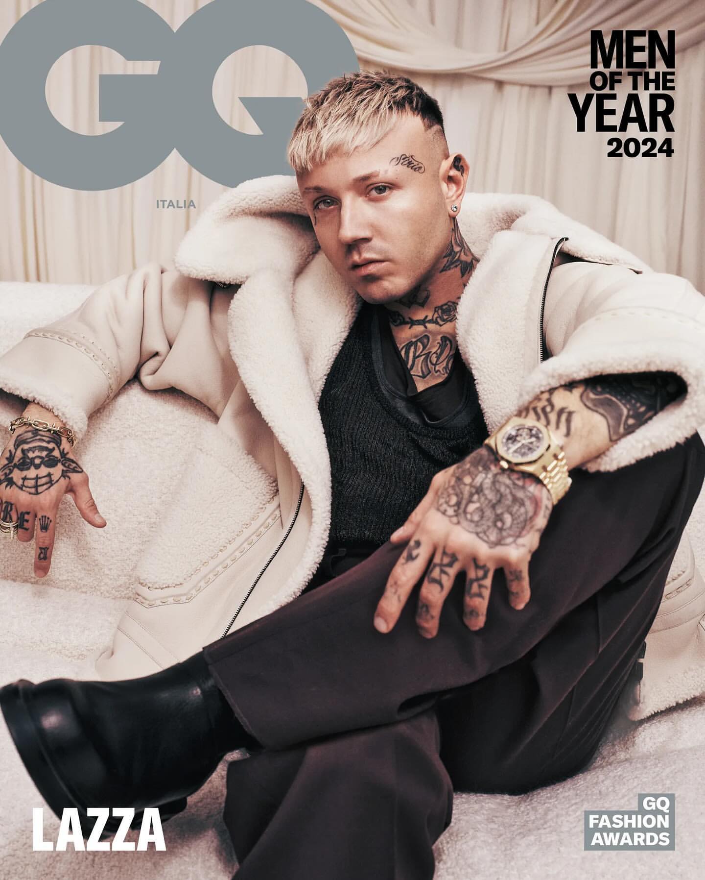 GQ magazine cover featuring platinum-haired model Lazza wearing a cream-colored coat, brown pants, and black boots, sitting on white fabric.