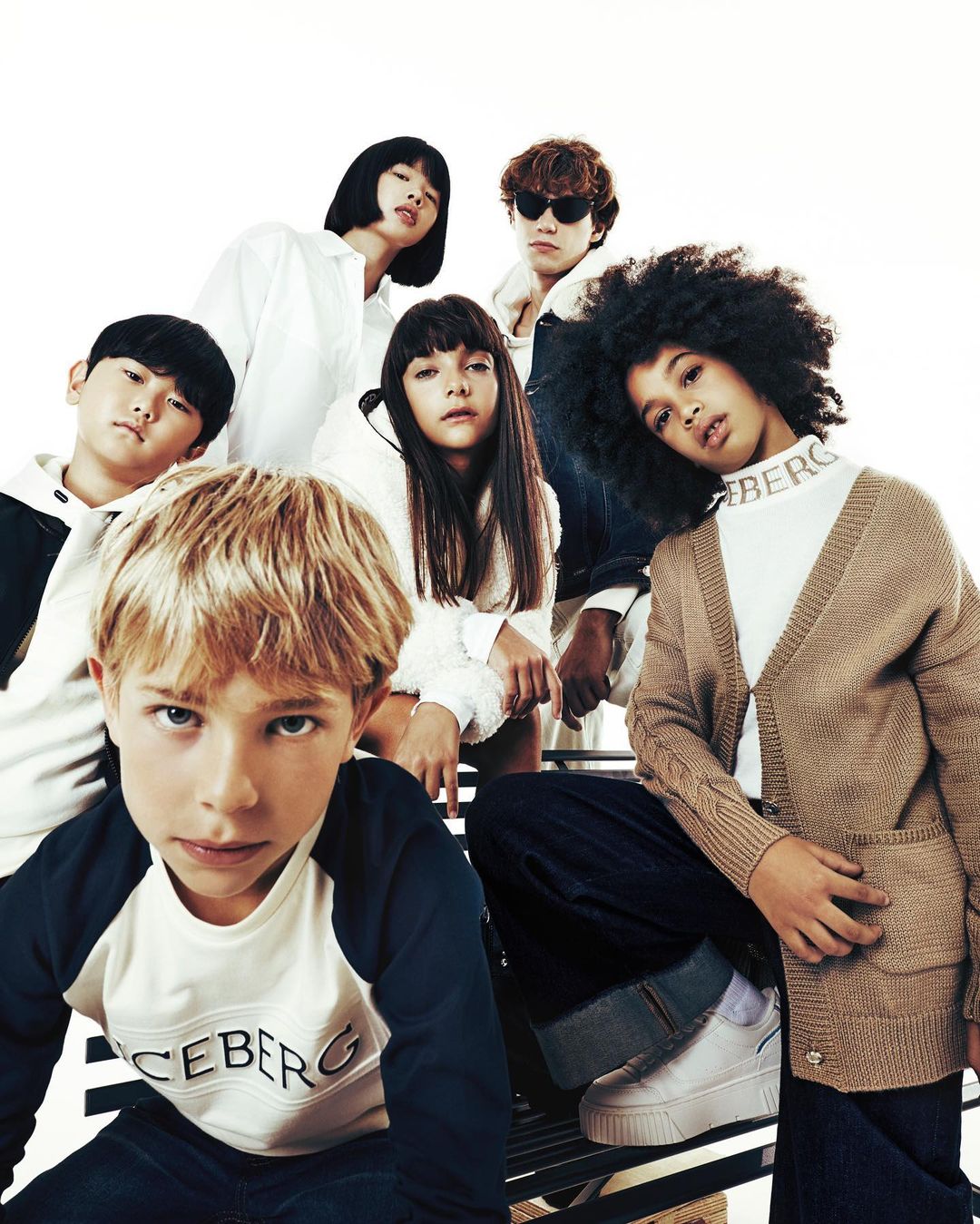 Group of children, girls and boys, wearing casual clothing with the Iceberg logo in a studio setting against a white backdrop.