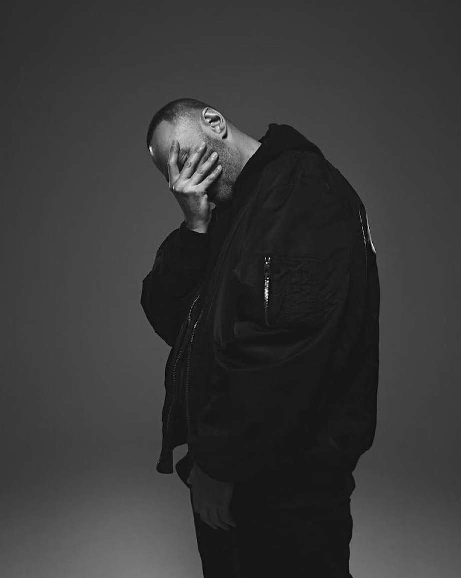 Black and white studio shot of a man wearing a jacket with his hand covering his face. Monochrome portrait on gray backdrop.