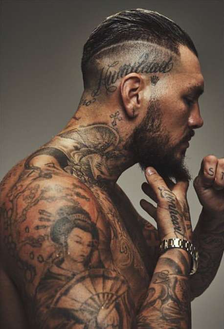 Profile shot of a muscular adult man with tattoos and an undercut hairstyle, posing shirtless in a photo studio with neutral background.